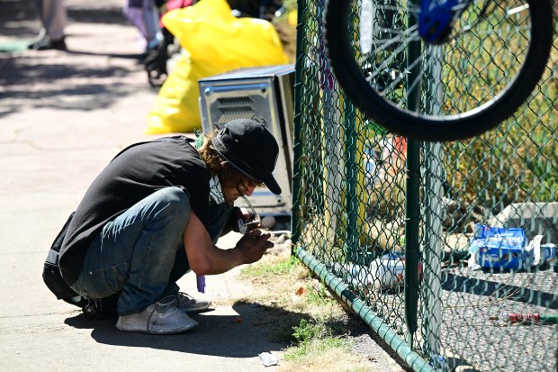 A man smokes drugs at an encampment along North Logan Street and East Eighth Avenue in Denver on Sept. 25, 2023.
